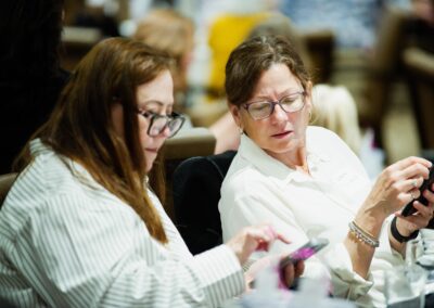 Two women on their phones helping each other at The Common Ground of Energy Transformation event