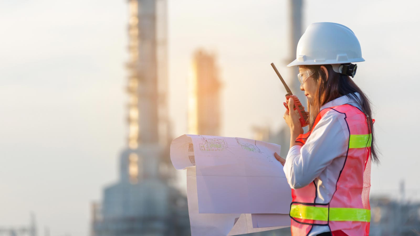 Woman with a hardhat and vest at a job site talking on a walkie-talkie